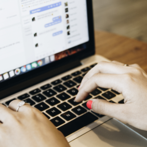 lakkozott körmű női kéz gyűrűvel a bal mutatóujján egy macbook billentyűzetén, a laptop képernyőjén a facebook van nyitva